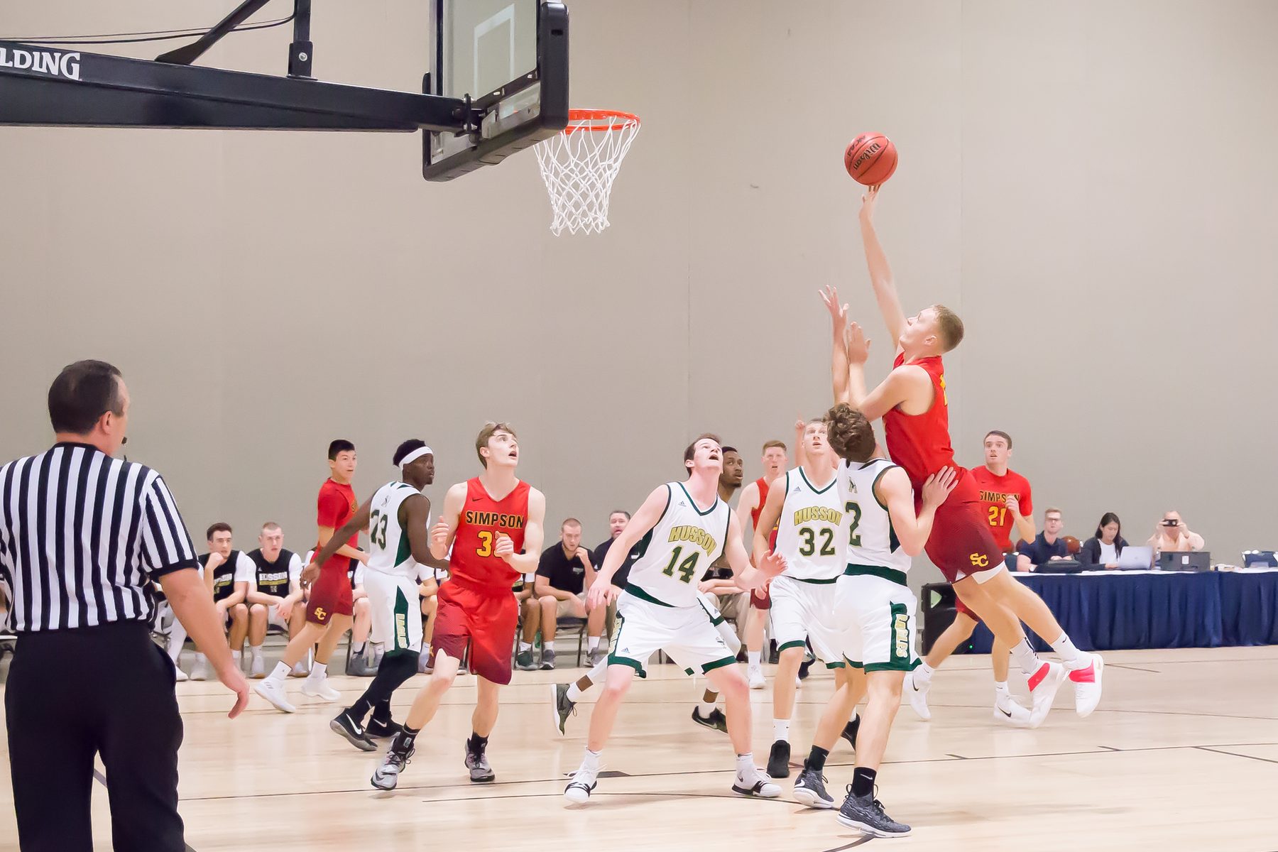 A basketball player in a red jersey jumps to shoot as defenders reach for the ball under the hoop at a Trip Sports event
